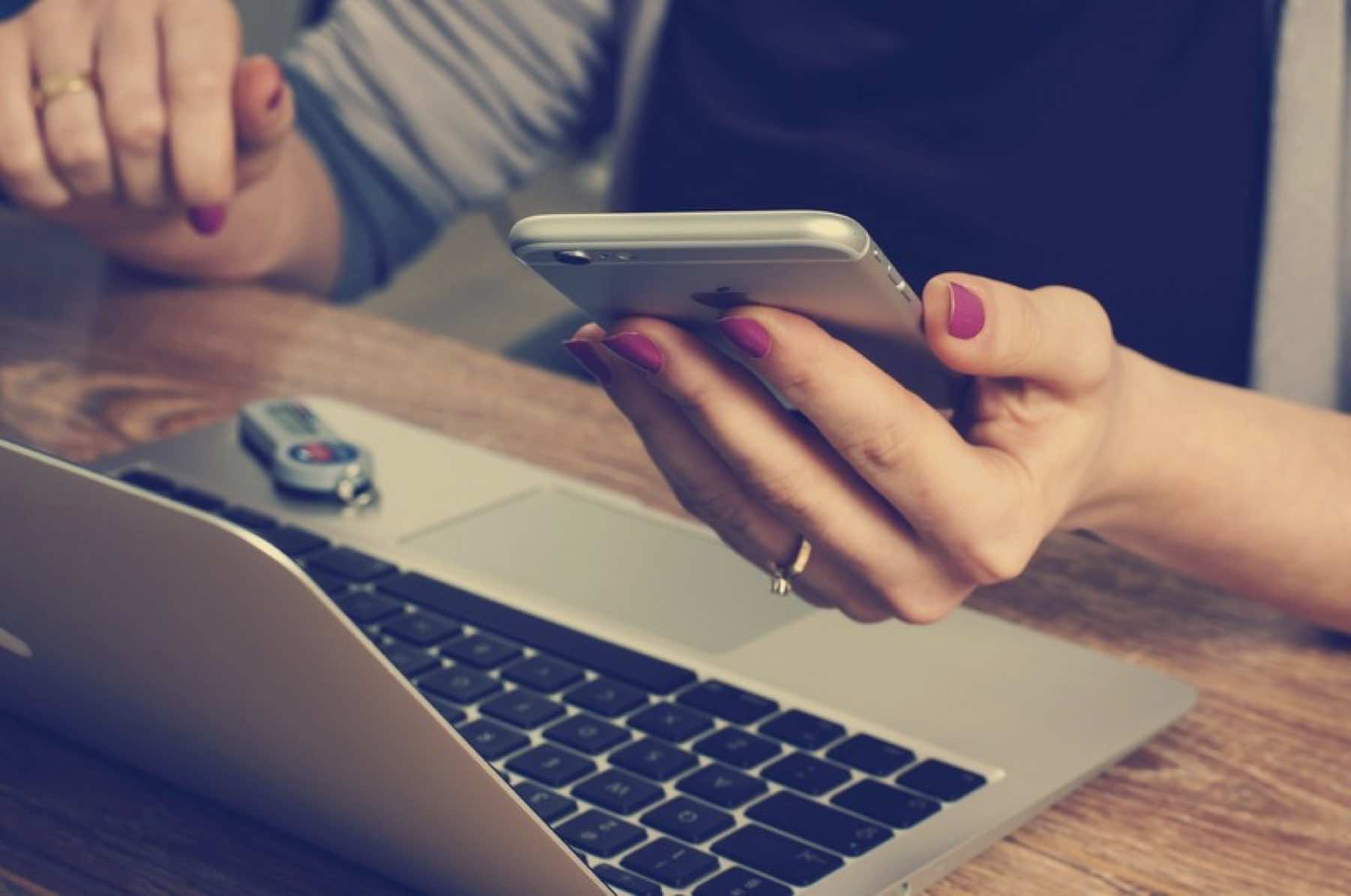 Femme devant son ordinateur, un smartphone à la main