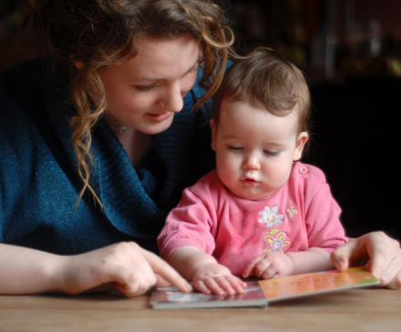 assistante maternelle regarde un livre avec un bébé